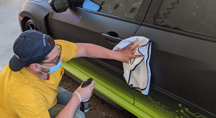 person applying vinyl protection spray with a hand cloth to a wrapped vehicle